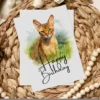 Delightful watercolor card featuring an Abyssinian cat in a natural setting, celebrating with a "Happy Birthday" message.