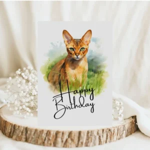 Watercolor birthday card featuring an Abyssinian cat in a natural setting with a cheerful "Happy Birthday" message.