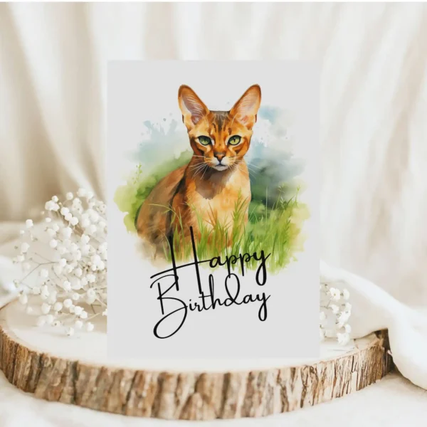 Watercolor birthday card featuring an Abyssinian cat in a natural setting with a cheerful "Happy Birthday" message.