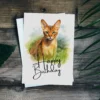 Watercolor illustration of an Abyssinian cat on a birthday card, set in nature, with a joyful "Happy Birthday" message.