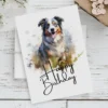 Cheerful birthday card for dogs, illustrating an Australian Shepherd in a watercolor landscape, with a "Happy Birthday" message.