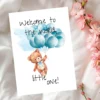 Watercolor card featuring a teddy bear with blue balloons and the message, "Welcome to the world, little one!"
