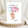 Cute teddy bear card featuring pink balloons and the phrase, "Welcome to the world, little one!" in a watercolor design.
