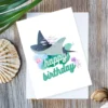 Watercolor manta ray birthday card with fish school and “Happy Birthday” message