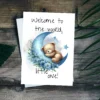 Charming bear on a blue moon in watercolor, featuring the message, "Welcome to the world, little one!" for new baby cards.