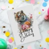 Happy birthday card featuring a cheerful tiger surrounded by colorful floral designs. Perfect for a fun celebration!