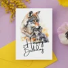 Happy birthday card design featuring a wolf mother and her pub in a colorful watercolor style.