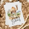 Cheerful watercolor camel birthday card set in nature, complete with a festive "Happy Birthday" inscription.