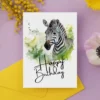 Happy birthday card featuring a zebra in a watercolor style, set in nature, with a joyful birthday greeting.